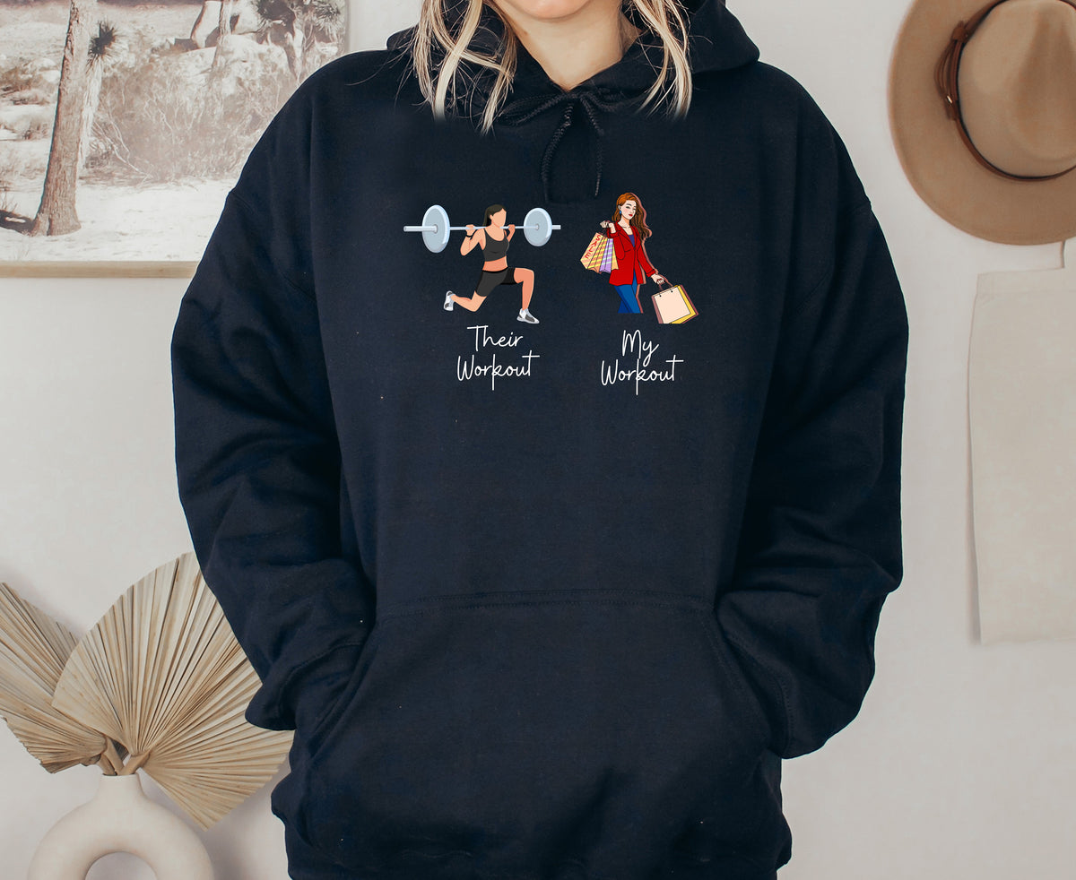 Funny Fitness Hoodie in black worn front-facing with lifter and shopper graphics beside wall art, hat and vase.