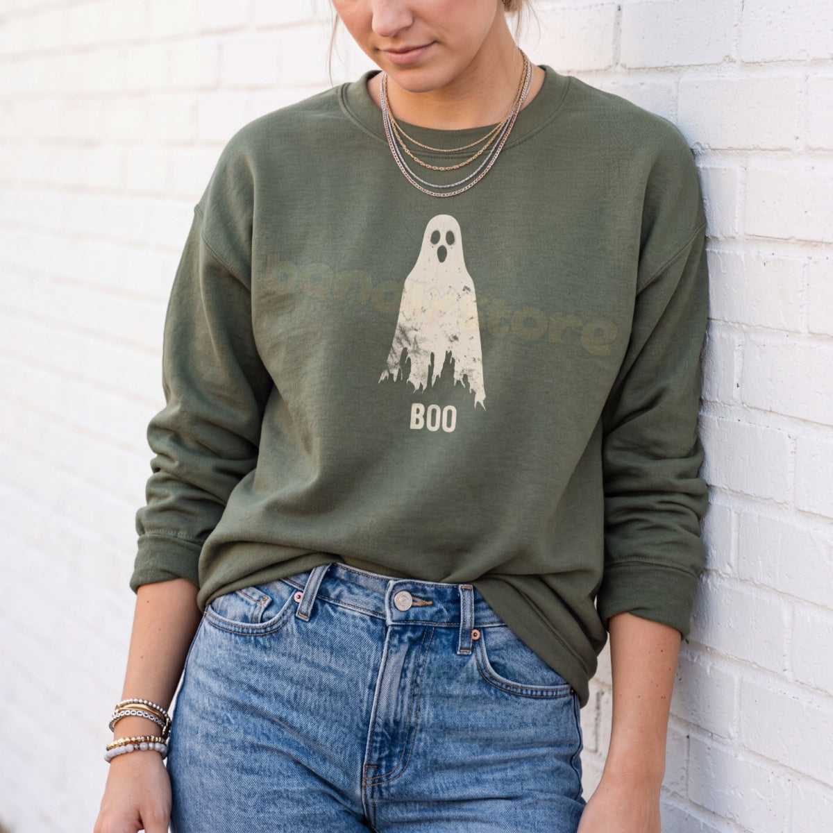 Grungy Ghost Sweatshirt in military green, worn front-facing by a person against a white brick wall.