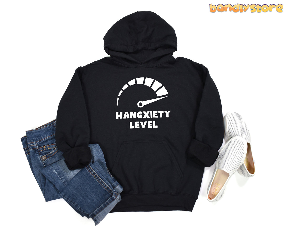 Hangxiety Hangover Hoodie in black laid flat beside blue jeans and white slip-on shoes.