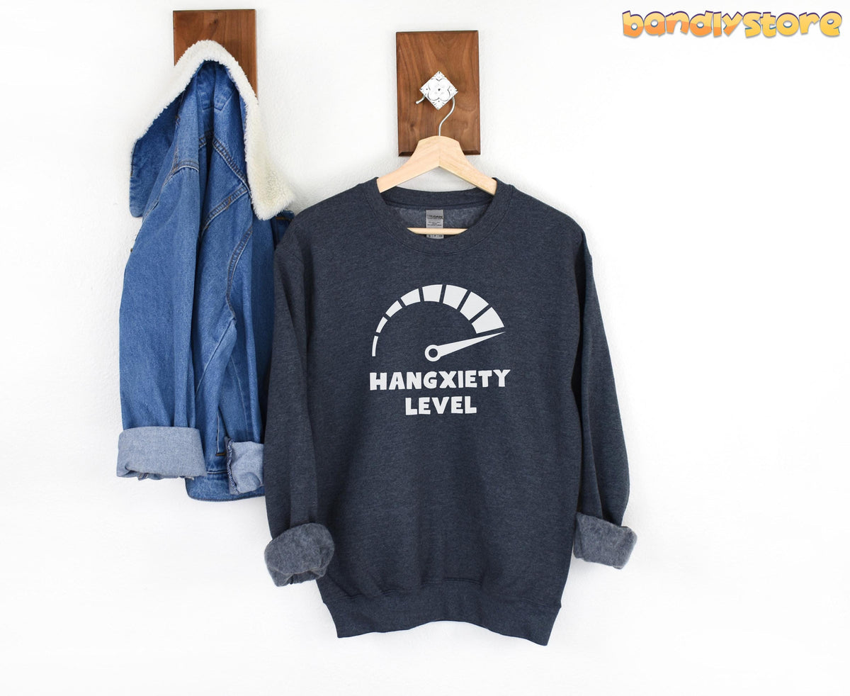 Hangxiety Hangover Sweatshirt in Dark Heather hanging on a wooden hanger on a white wall beside a denim jacket.