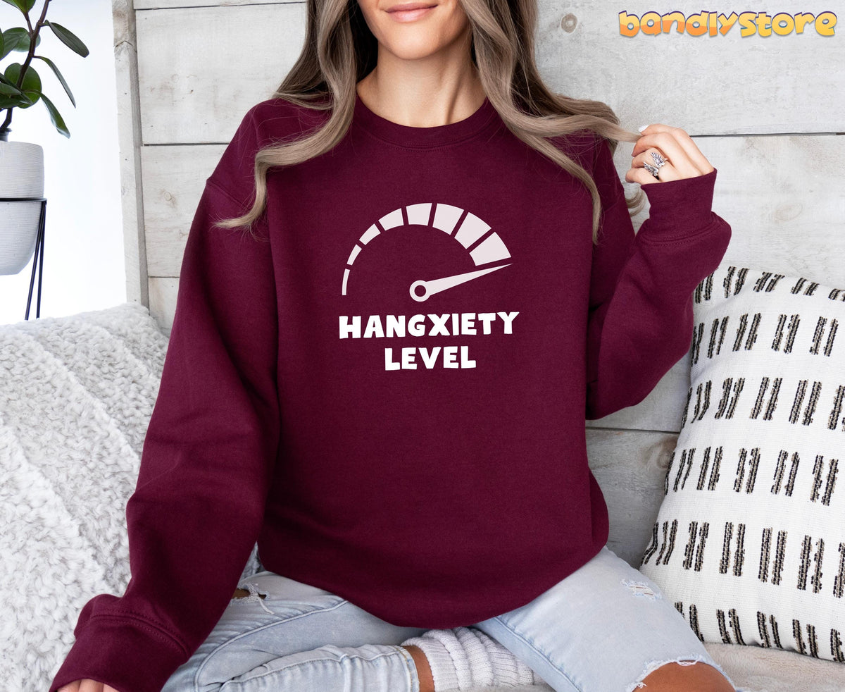Hangxiety Hangover Sweatshirt in maroon on a woman seated by wooden wall with plant and pillows.