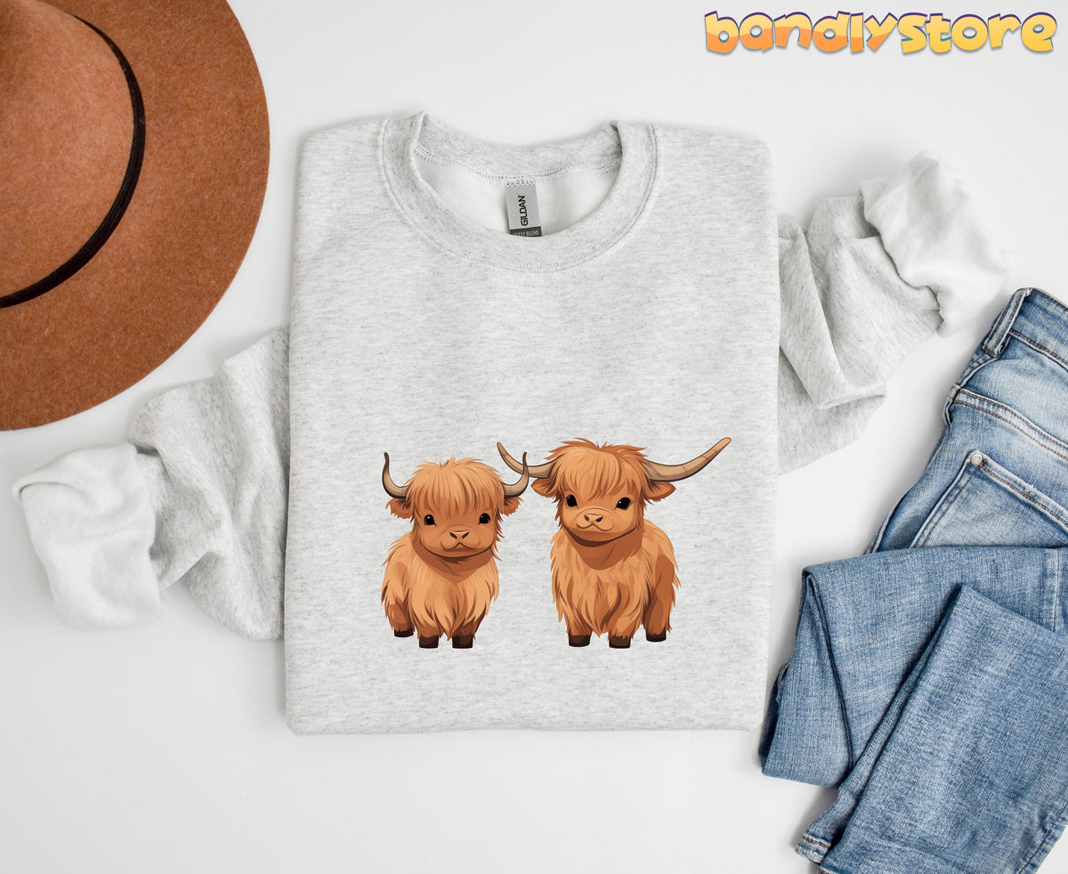 Highland Cow Sweatshirt in ash flat-laid from above beside a brown hat and blue jeans.