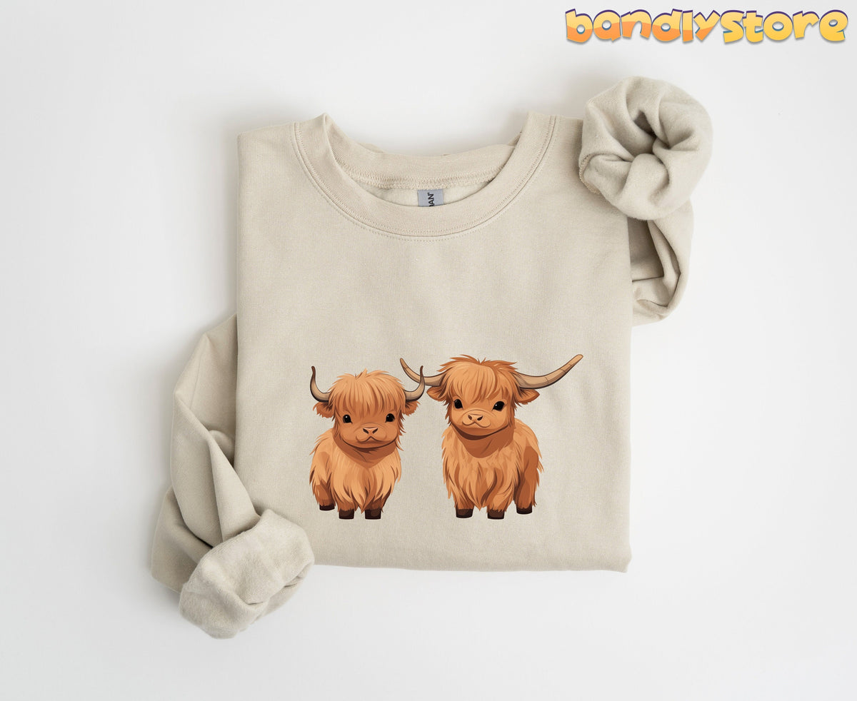 Highland Cow Sweatshirt in sand folded flat on a plain white background with two highland cows.