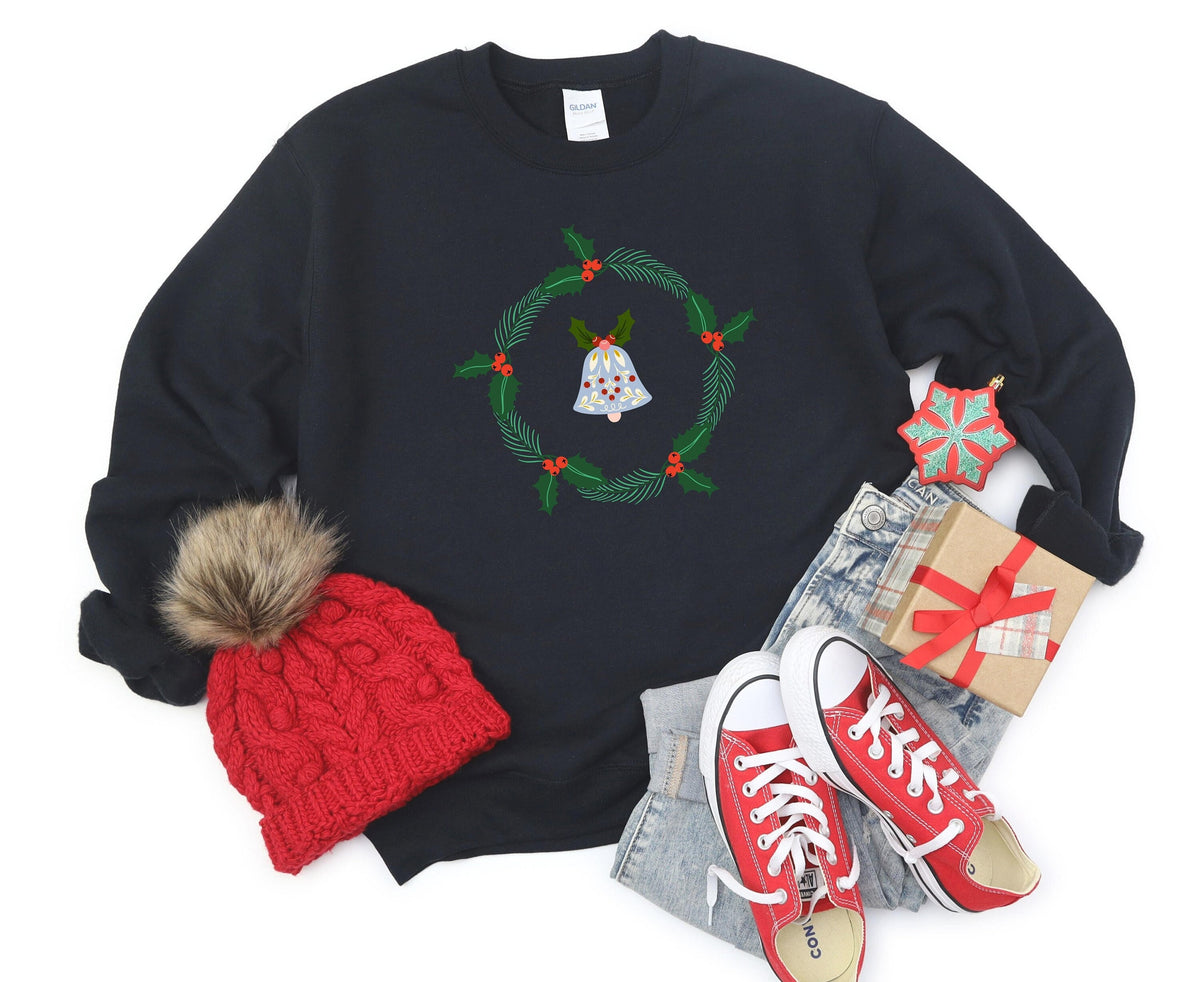 Holly Wreath Sweatshirt on black fabric, flat-laid with red beanie, red sneakers, jeans, gift box and snowflake ornament.