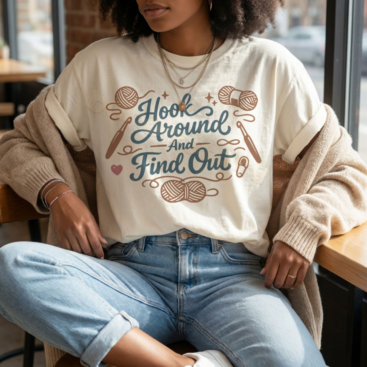 Hook Around And Find Out T-Shirt in ivory on a seated wearer in a cafe by a window with cardigan and jeans.