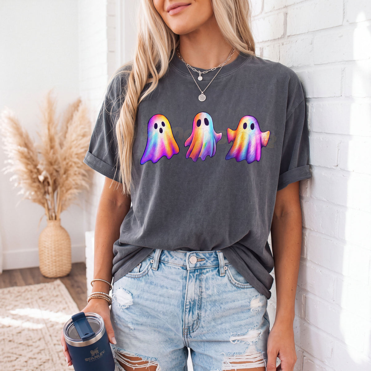 Iridescent Ghosts T-Shirt in Pepper worn by a woman leaning against a white brick wall holding a tumbler.