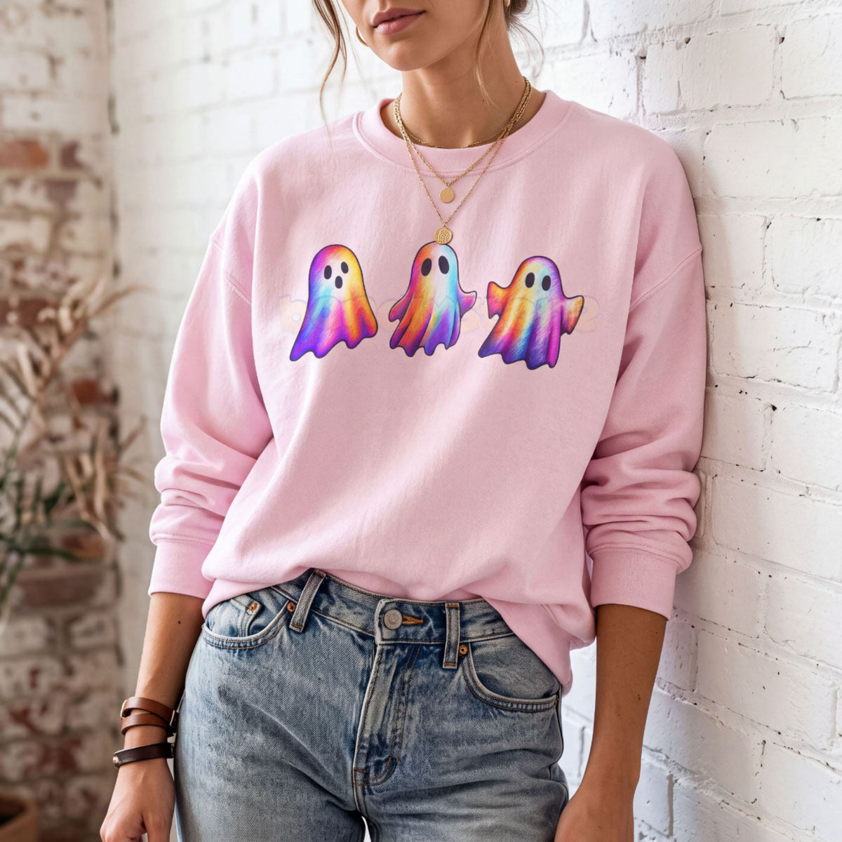 Iridescent Ghosts Sweatshirt in light pink worn by a person leaning against a white brick wall.