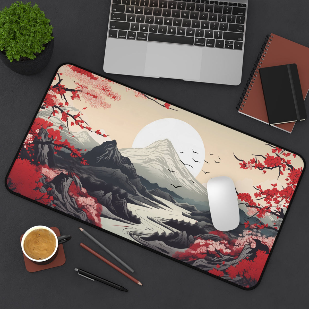 Japanese Mountains Desk Mat in 12 ร 22 inches lies top-down on a desk with laptop, plant, notebooks, mouse and coffee.
