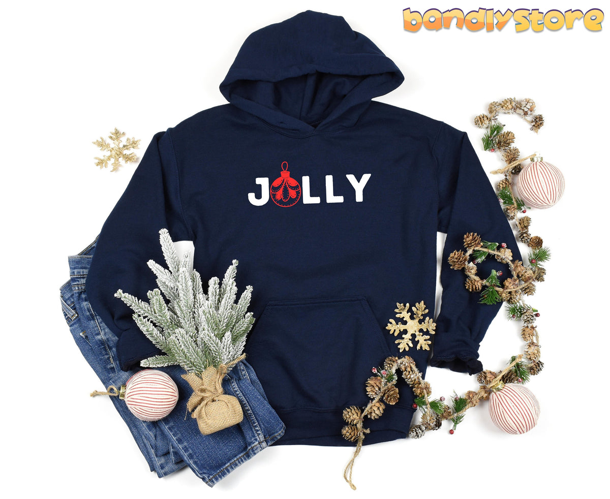 Feeling Jolly Christmas Hoodie in navy laid flat beside jeans, frosted mini tree, pinecone garland and ornaments.