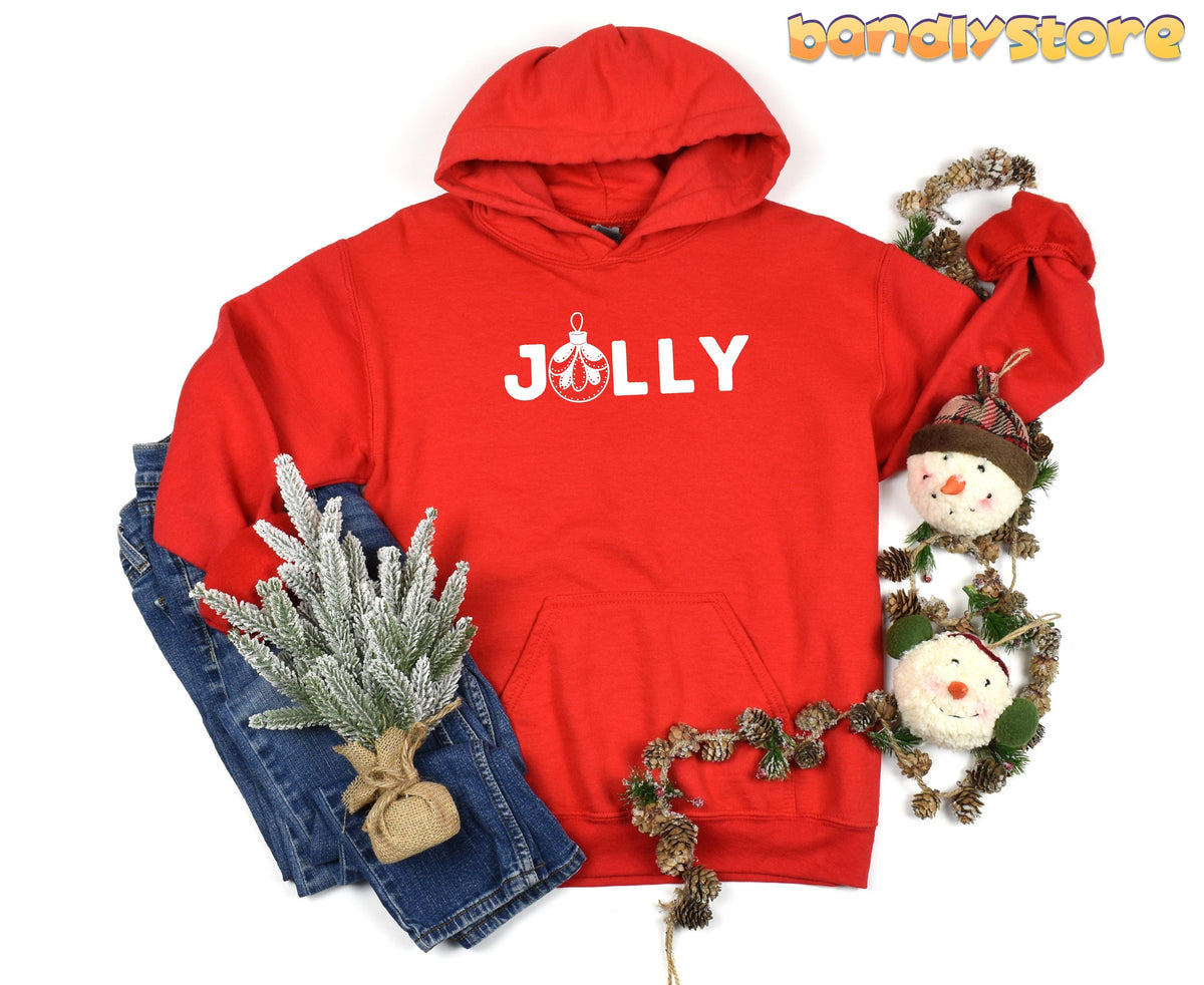 Feeling Jolly Christmas Hoodie in red, flat-lay with jeans, frosted greenery, pinecone garland and snowman ornaments.