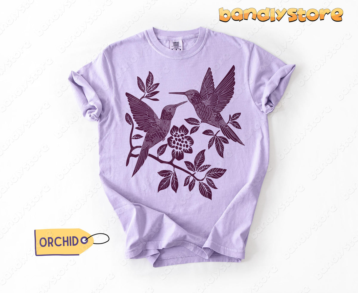 Linocut Hummingbird T-Shirt in orchid laid flat on white background with two hummingbirds and flower.