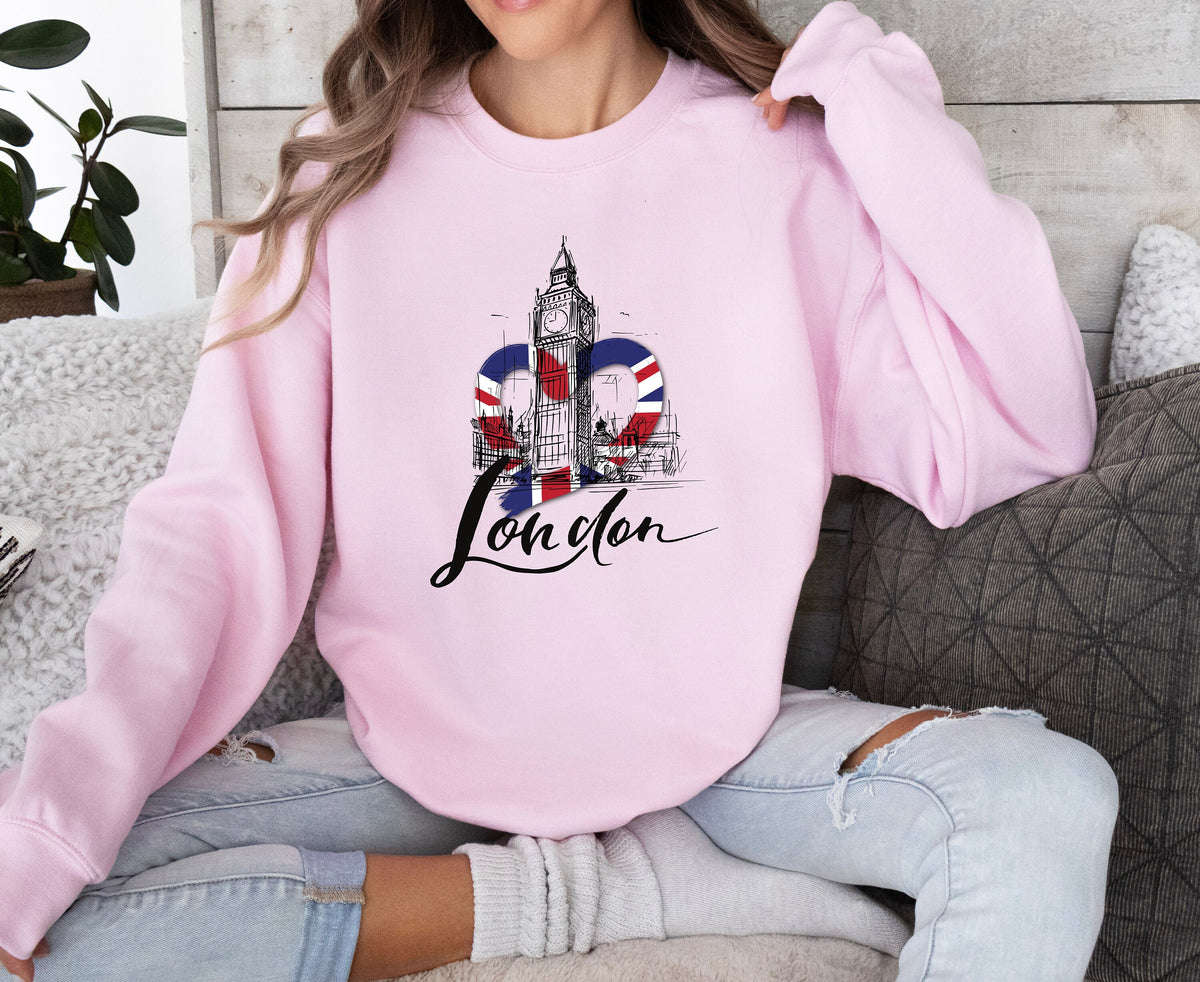 London Big Ben Sweatshirt in light pink worn by a seated woman on a sofa with pillows and a plant nearby.