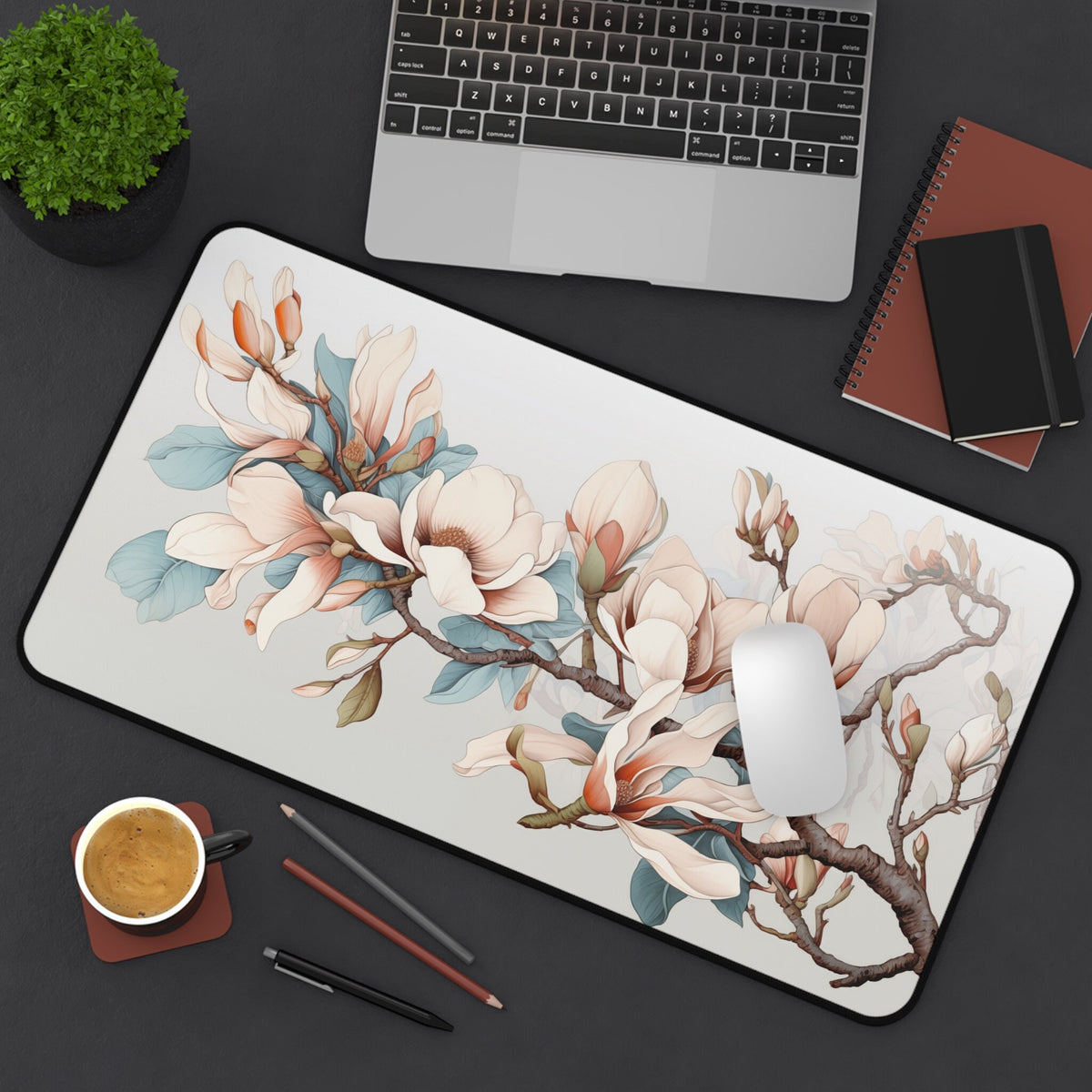 Magnolia Flowers Desk Mat in 12 × 22 inches shown top-down on a desk with laptop, plant, mouse, coffee cup and pens.