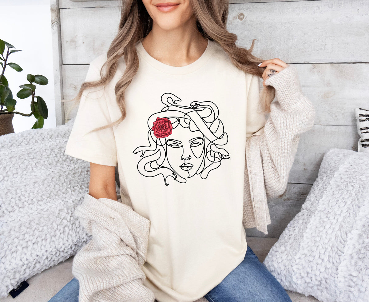 Medusa Head T-Shirt in natural on a seated person amid fluffy pillows and a plant by a wooden wall.