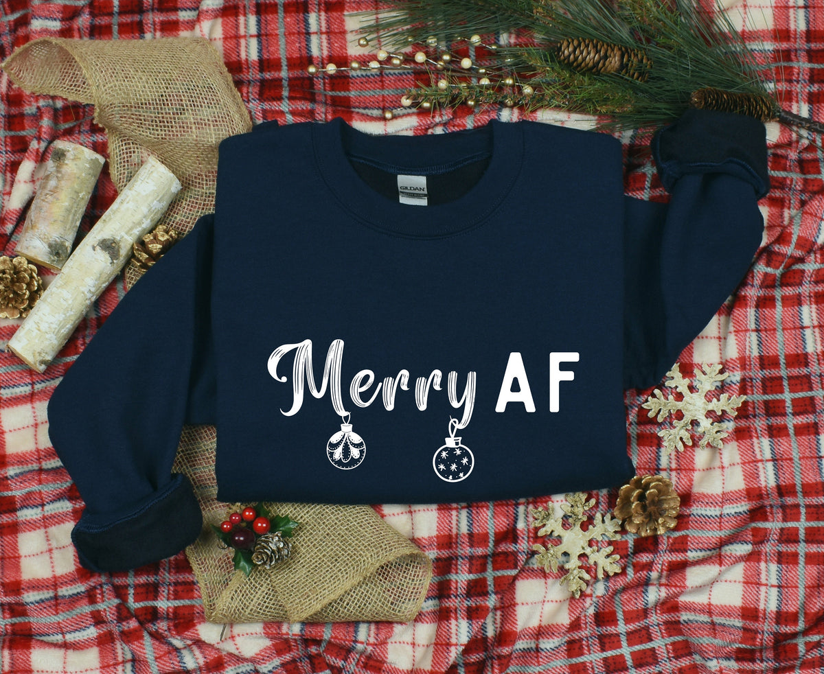 Merry AF Christmas Sweatshirt in navy laid flat on red plaid with pine, cones, birch and burlap.