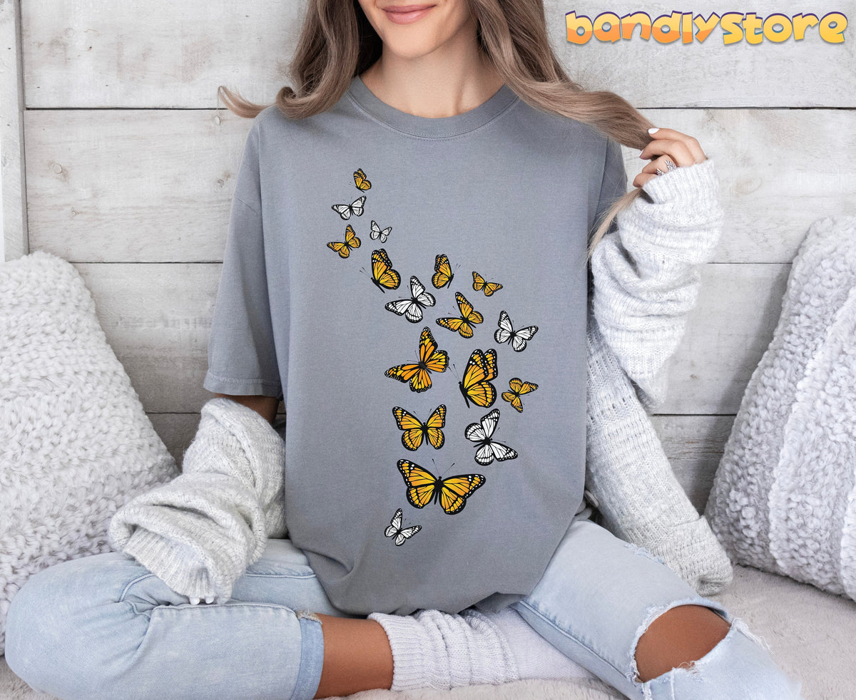 Monarch Butterfly Flock T-Shirt in grey on a seated model against wooden wall with white pillows