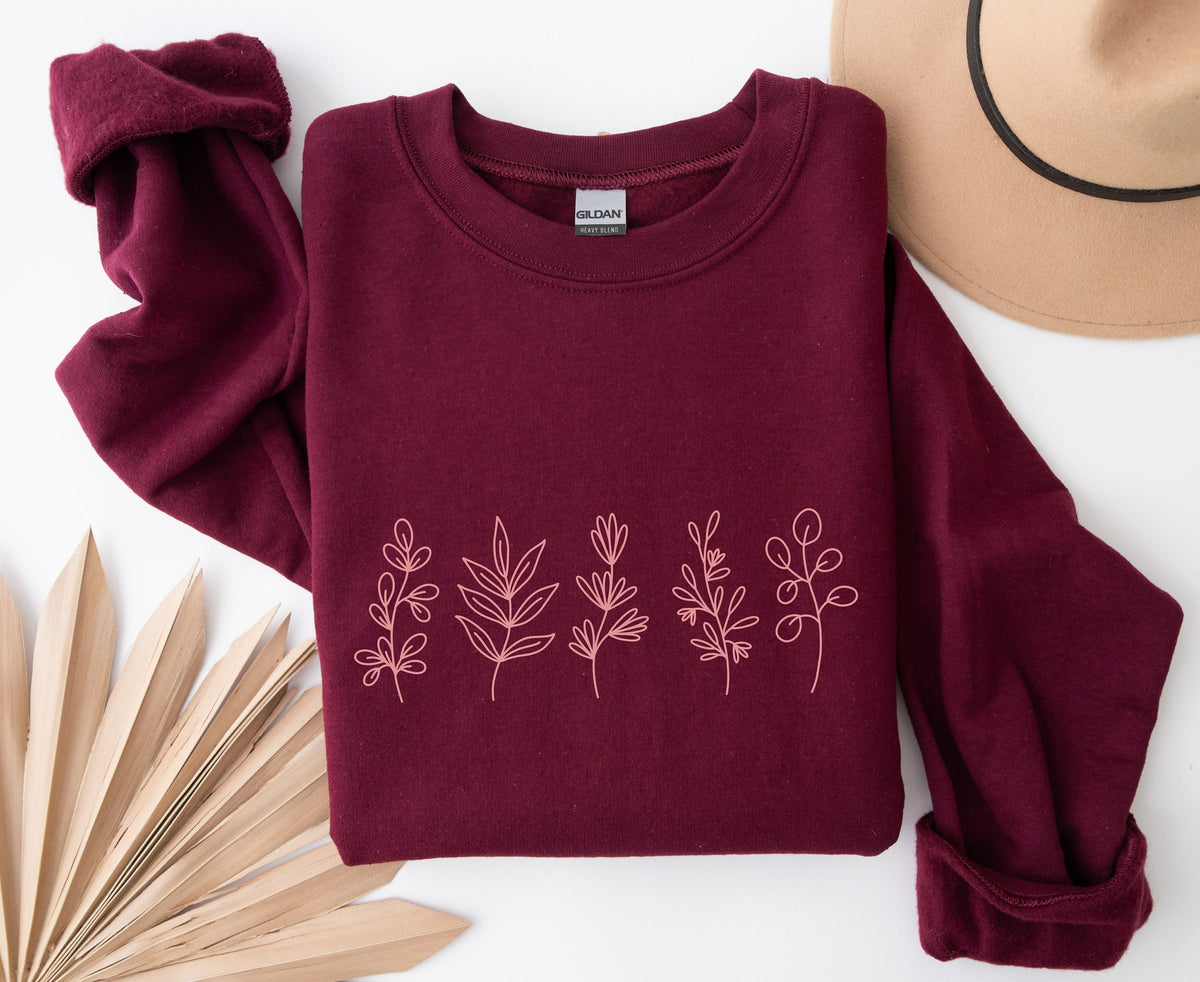 Monochrome Floral Sweatshirt in maroon folded flat beside a hat and dried leaves on white.