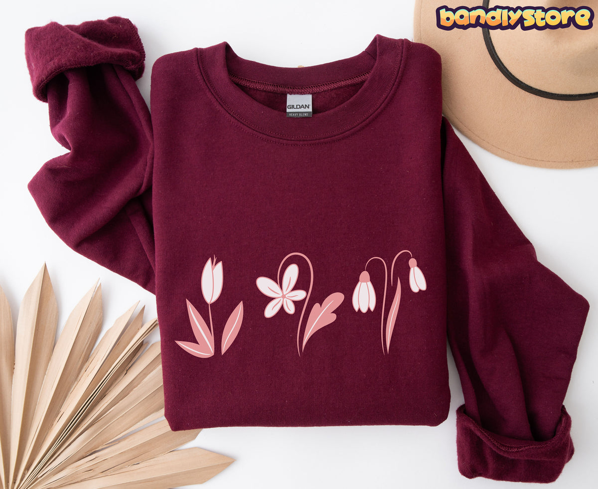 Monochrome Spring Flowers Sweatshirt in maroon folded flat from above beside a hat and dried leaves.