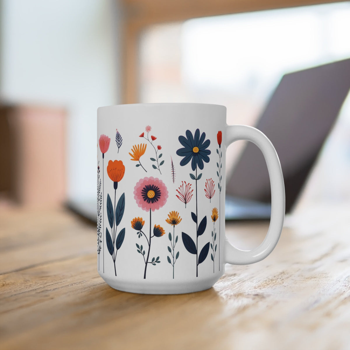 Navy Daisy Doodle Wildflowers Mug on a wooden table with a blurred laptop behind, handle angled right.