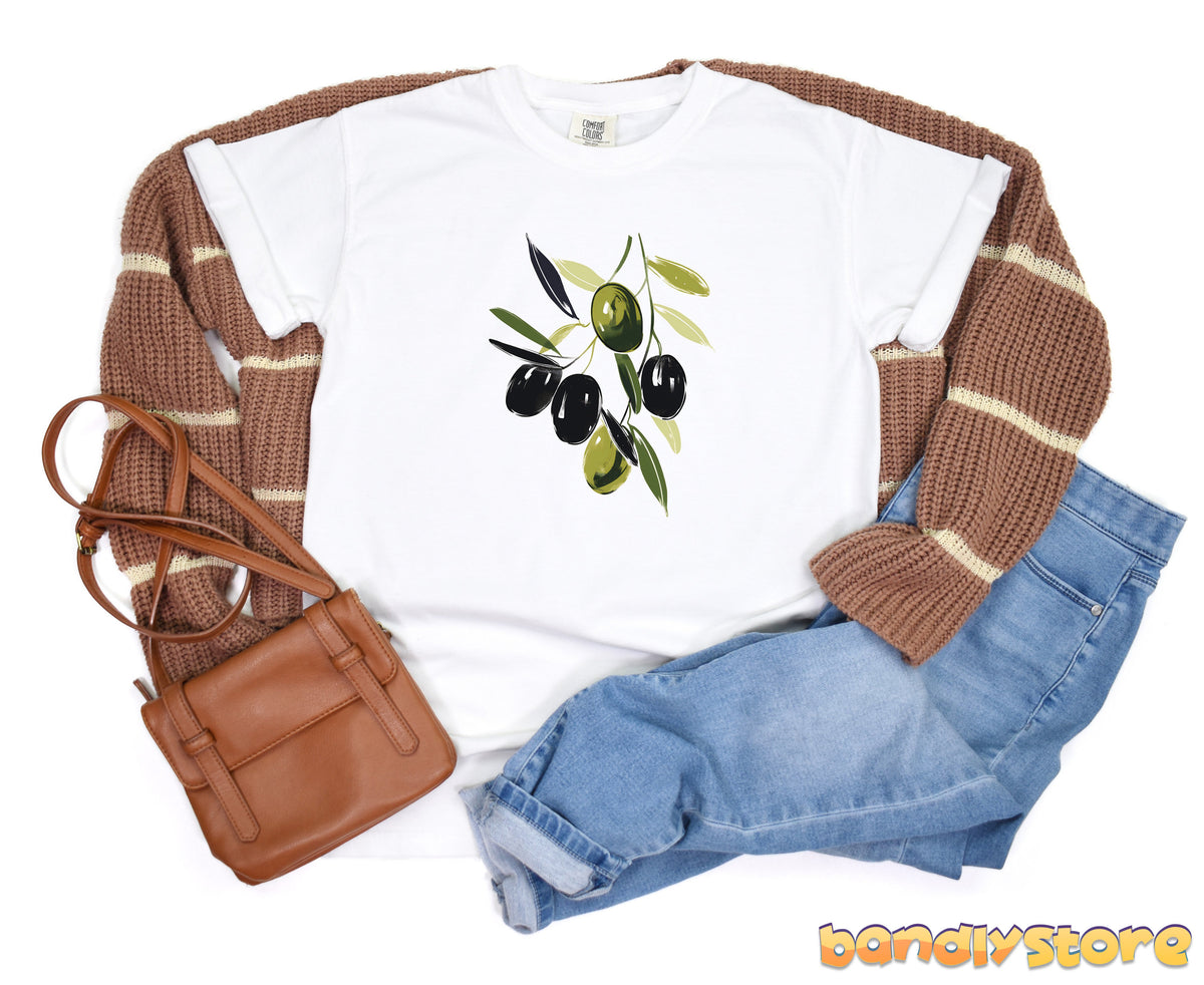 Olive Branch T-Shirt in white laid flat over a brown sweater beside a brown bag and blue jeans.