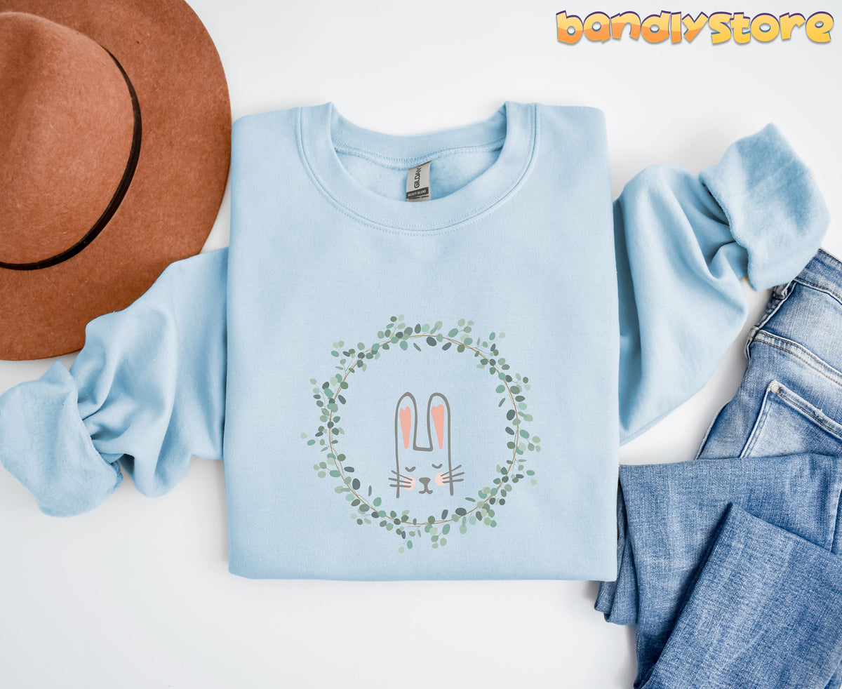 Spring Wreath Bunny Sweatshirt in light blue, overhead flat lay beside brown hat and jeans.
