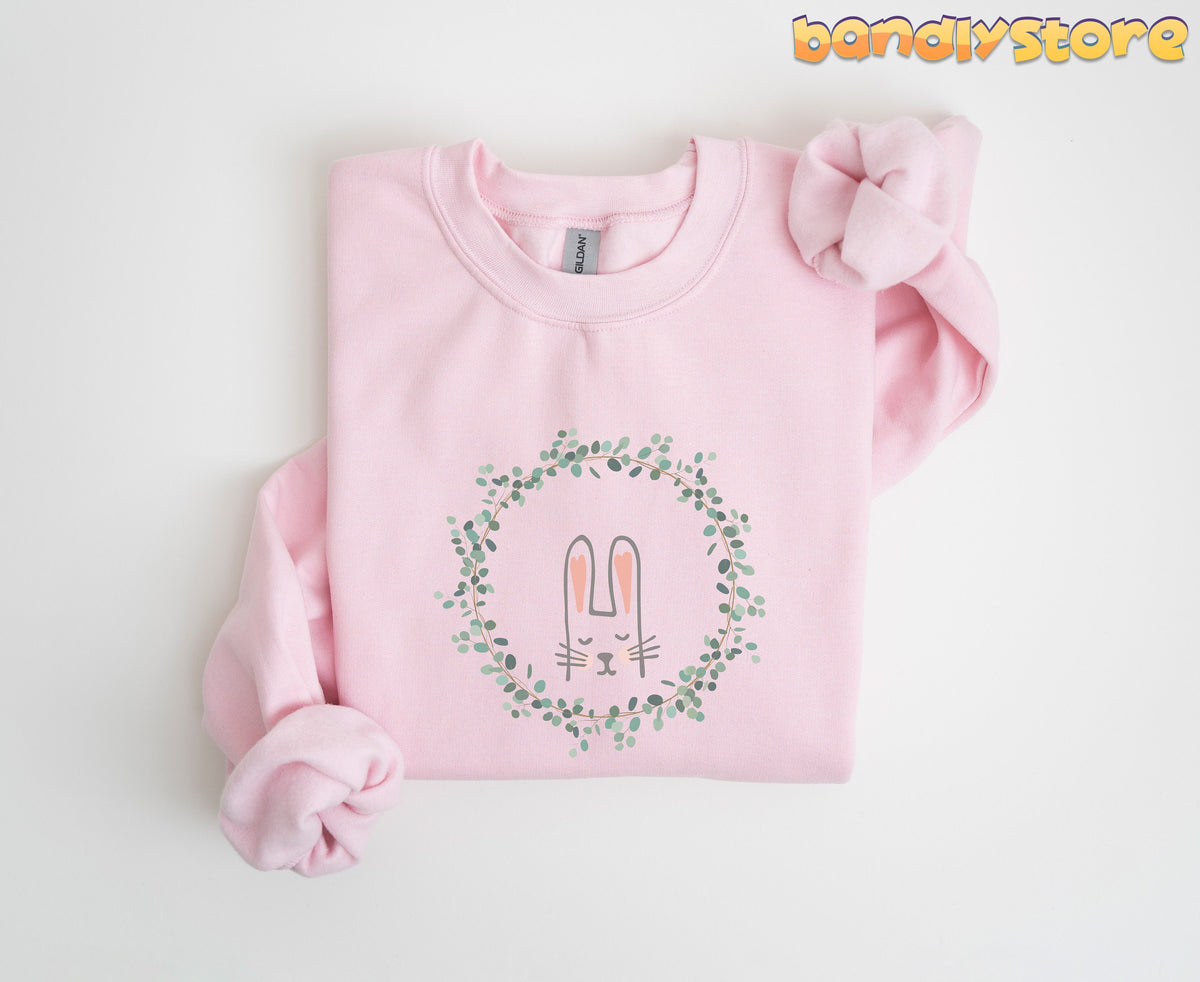 Spring Wreath Bunny Sweatshirt light pink folded flat on white with sleeves knotted, green leaf wreath and bunny face print.