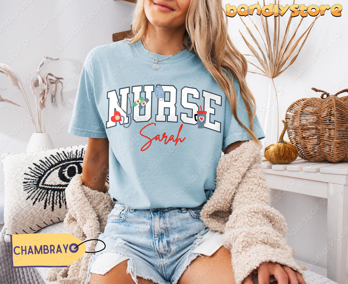 Personalized Nurse T-Shirt in chambray, front view on seated woman beside plants, pillow and pumpkins.