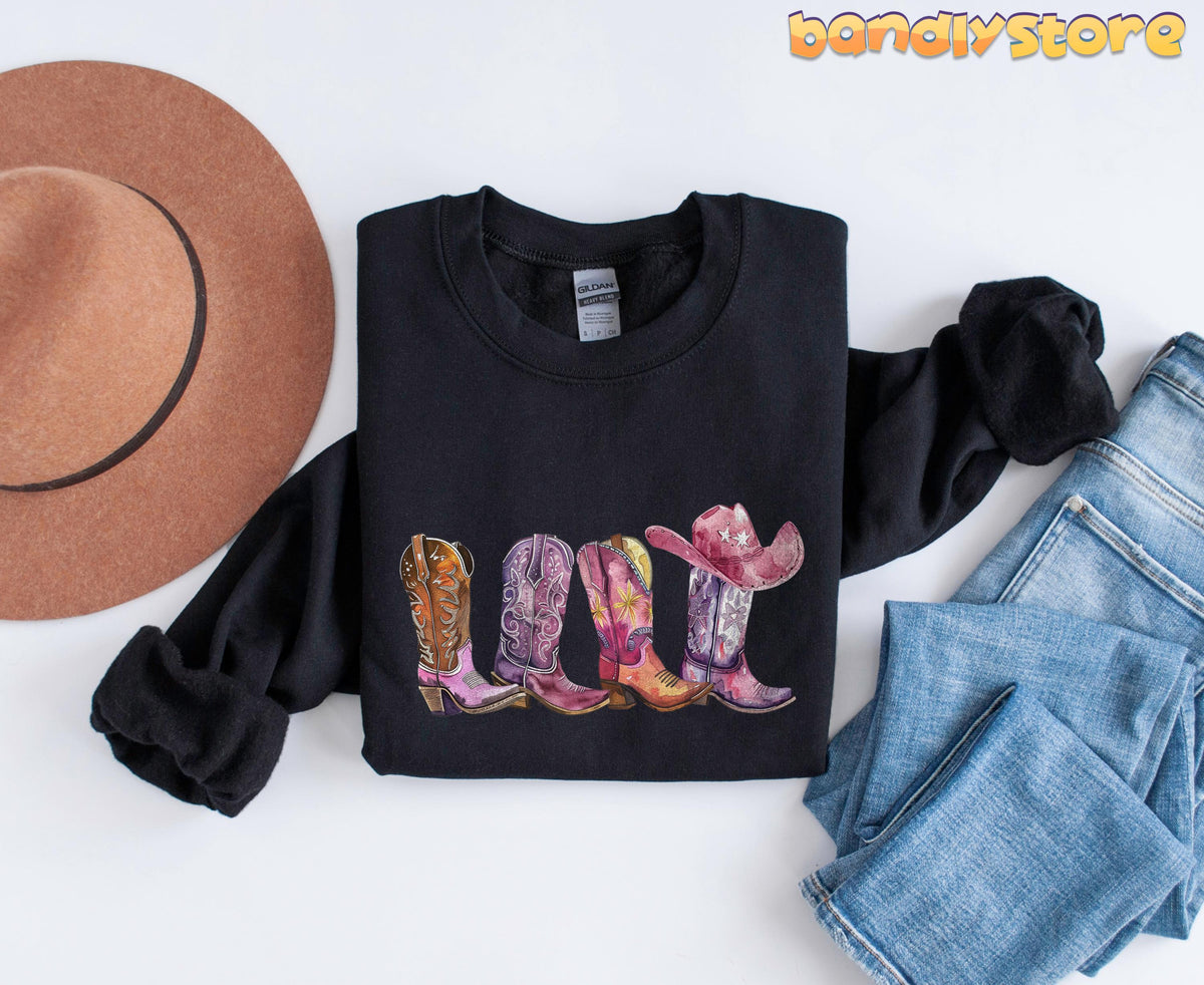 Pink Cowgirl Boots Sweatshirt black laid flat beside a brown hat and blue jeans.