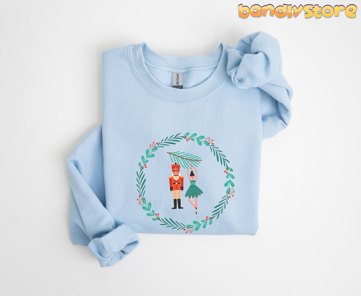 Nutcracker Ballet Sweatshirt in light blue, folded flat with a knotted sleeve beside a festive wreath graphic.