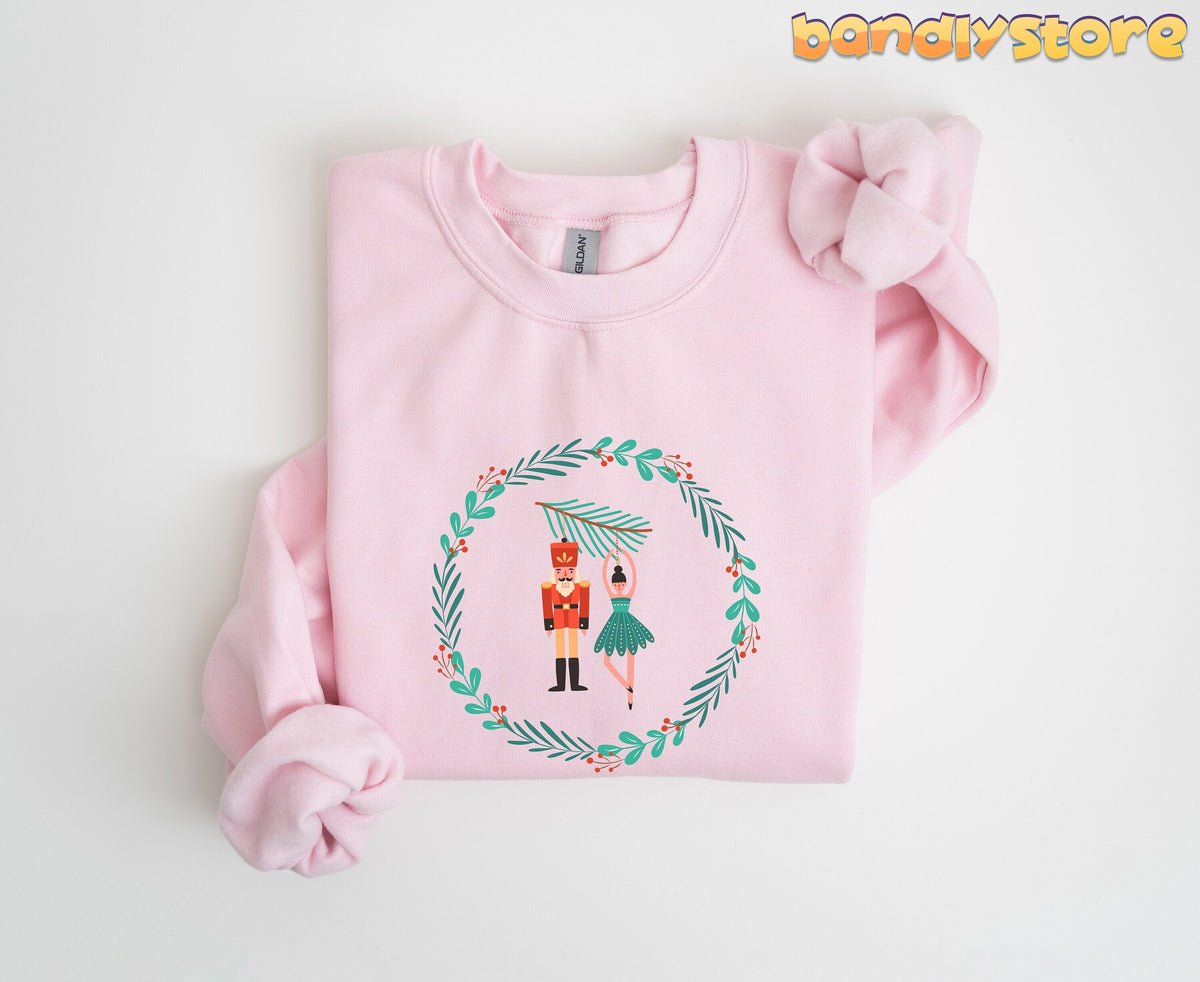 Nutcracker Ballet Sweatshirt in light pink, folded flat with a knotted sleeve and a holiday wreath graphic of nutcracker and ballerina.