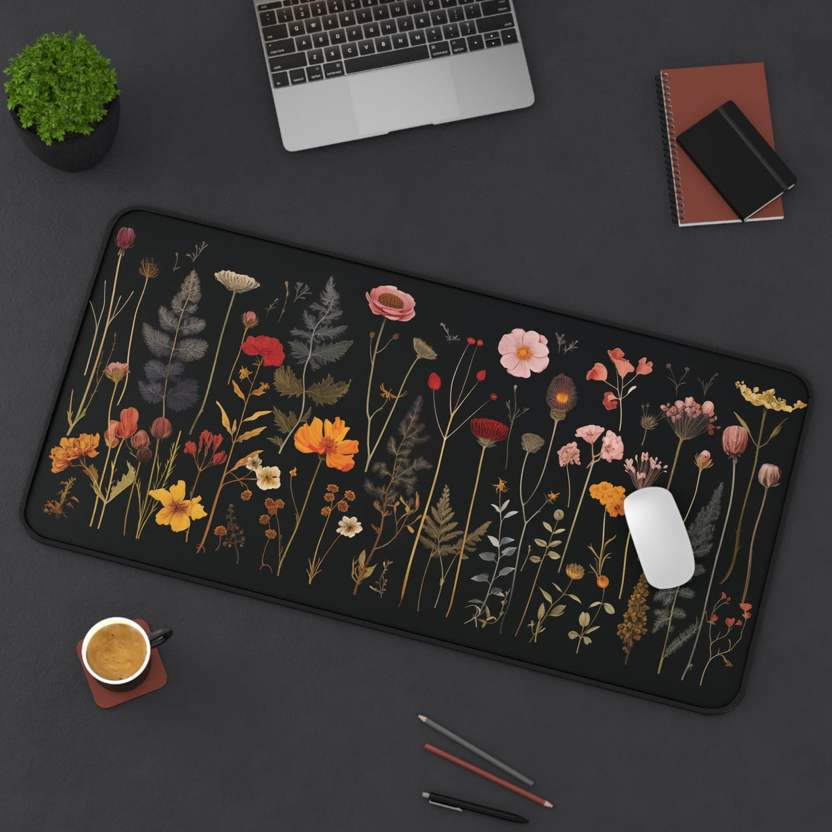 Pressed Wildflowers Desk Mat 16 ร 32 inches overhead on dark desk with laptop, plant, notebooks, coffee, pencils, mouse.