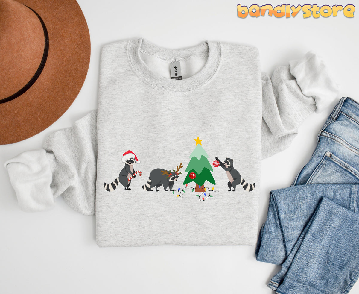 Raccoon Christmas Sweatshirt in ash, top-down flat lay beside a brown hat and blue jeans.
