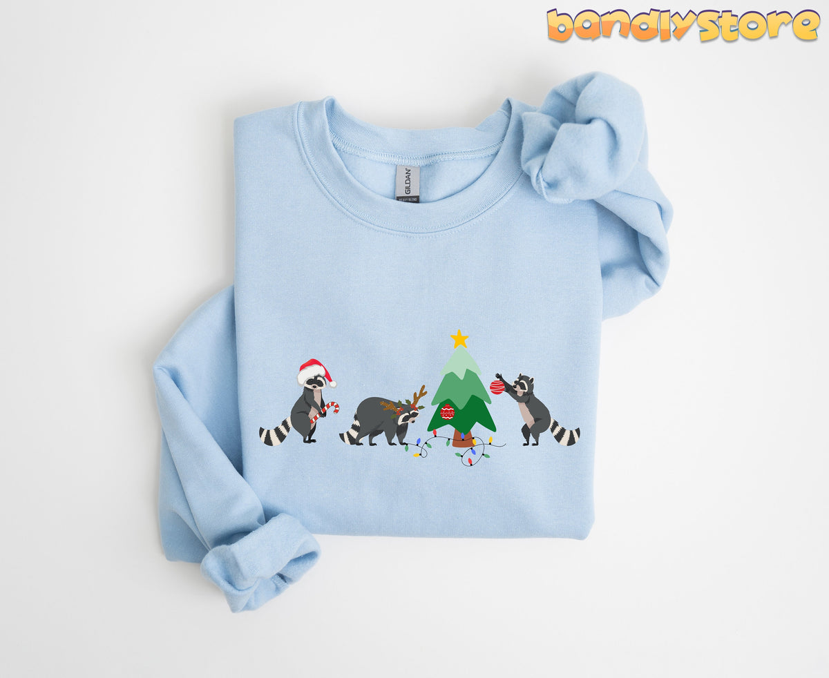 Raccoon Christmas Sweatshirt light blue folded on white background showing raccoons decorating a tree.