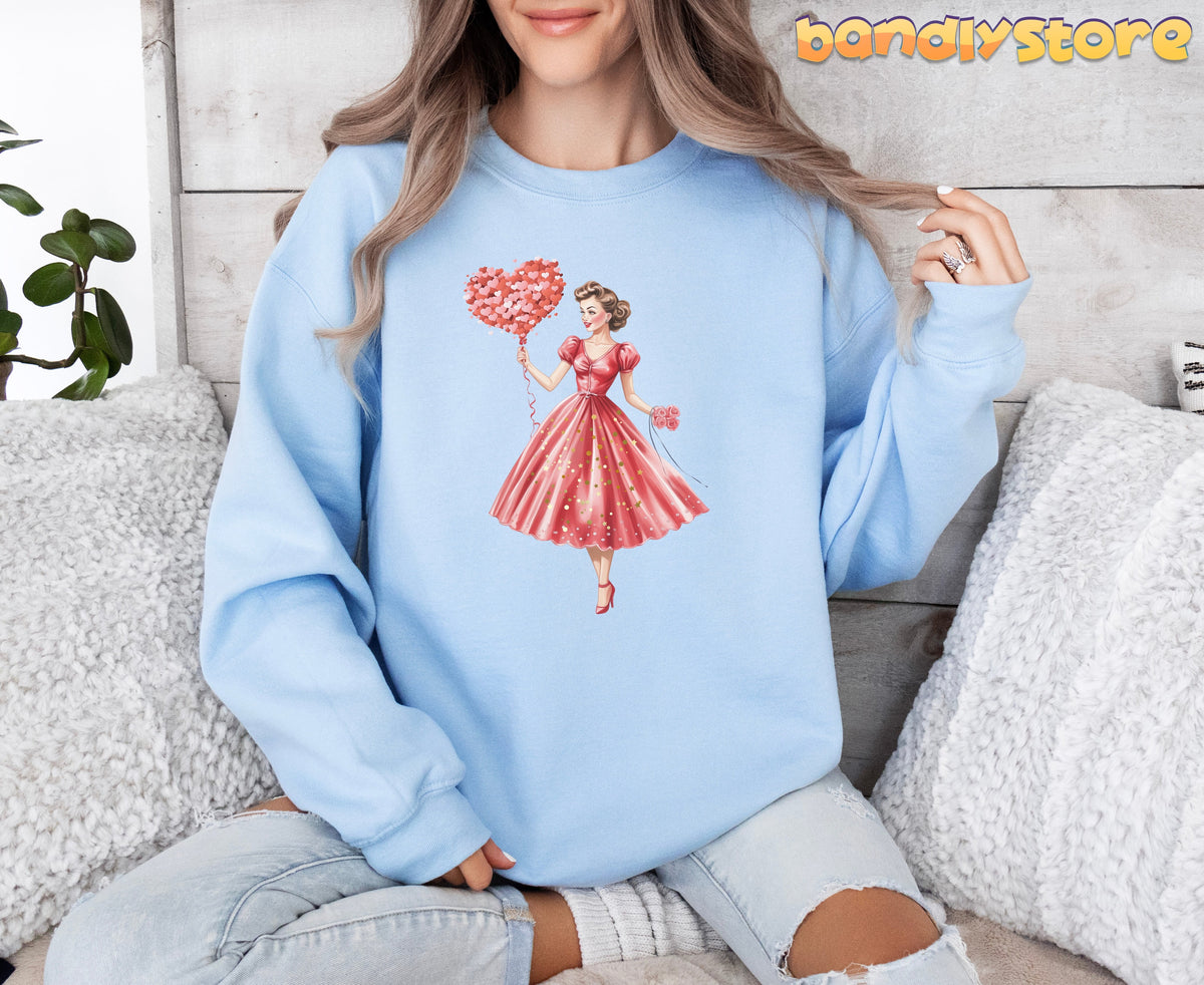 Cute Valentine Girl Sweatshirt on light blue fabric, model seated amid pillows and plants against wood wall.