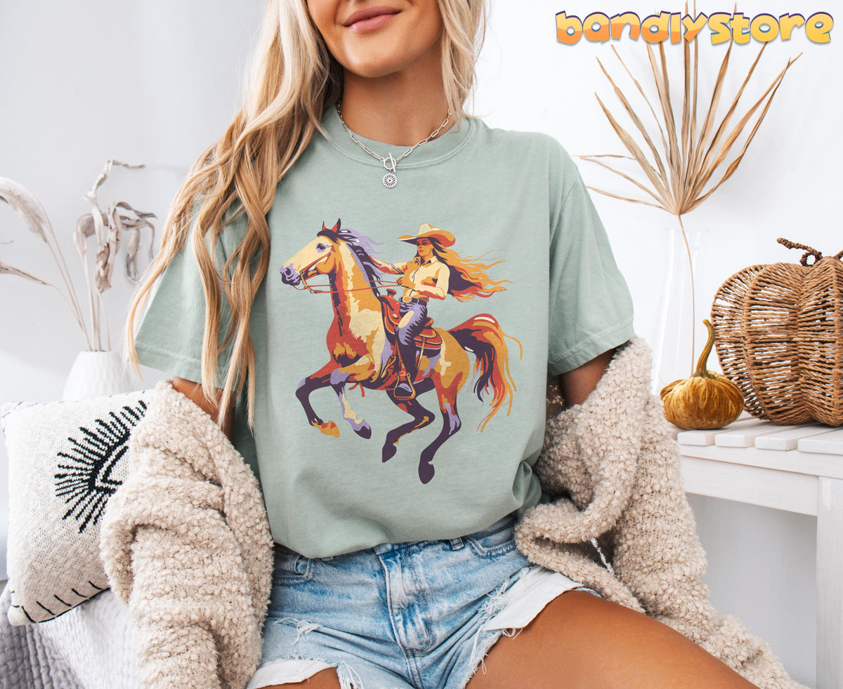 Retro Yeehaw Cowgirl T-Shirt in Bay on seated model, front view amid dried plants, pillow, pumpkin and basket.