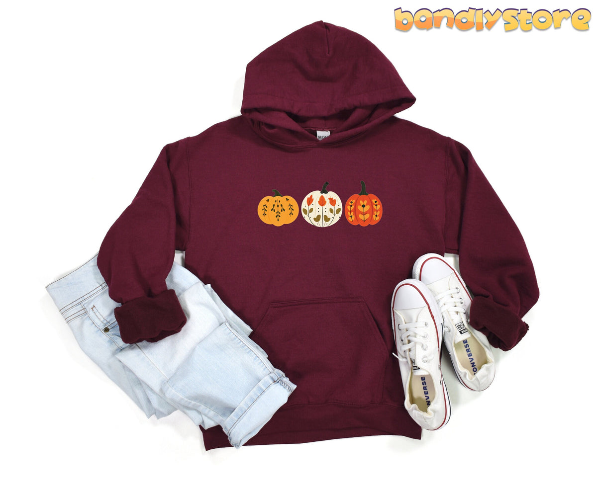 Scandinavian Art Pumpkin Hoodie in maroon laid flat beside folded jeans and white sneakers.