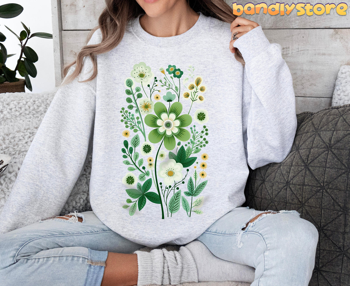 Scandinavian Wildflowers Sweatshirt in ash worn front-facing by a seated person on a couch with pillows and a plant.