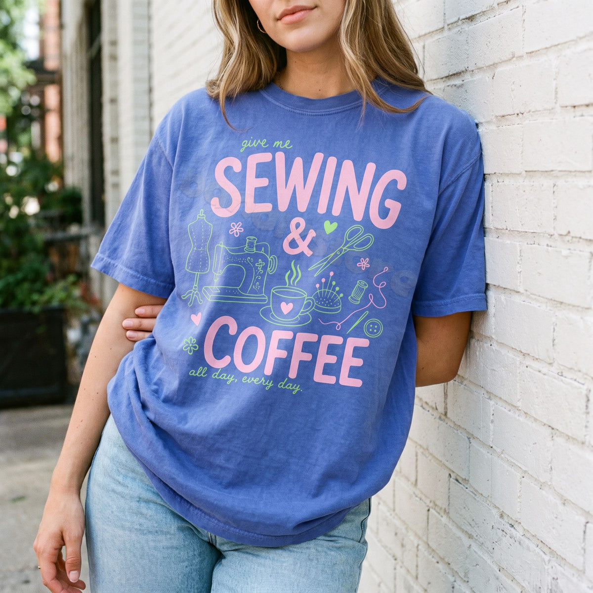 Sewing And Coffee T-Shirt in Flo Blue on a person leaning against a white brick wall outdoors.