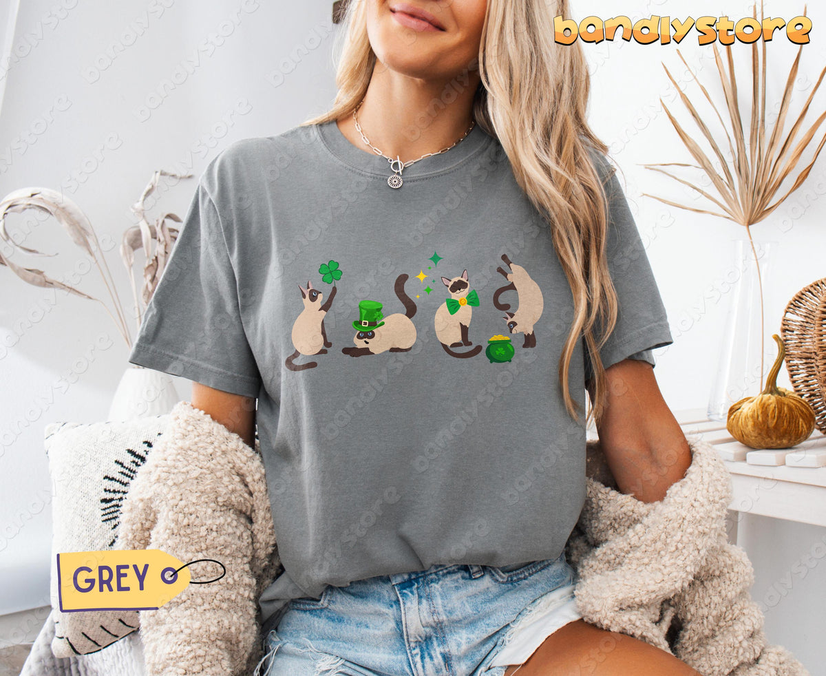 Siamese Cat Shamrock T-Shirt in grey worn by a seated woman indoors amid dried plants and pillows.