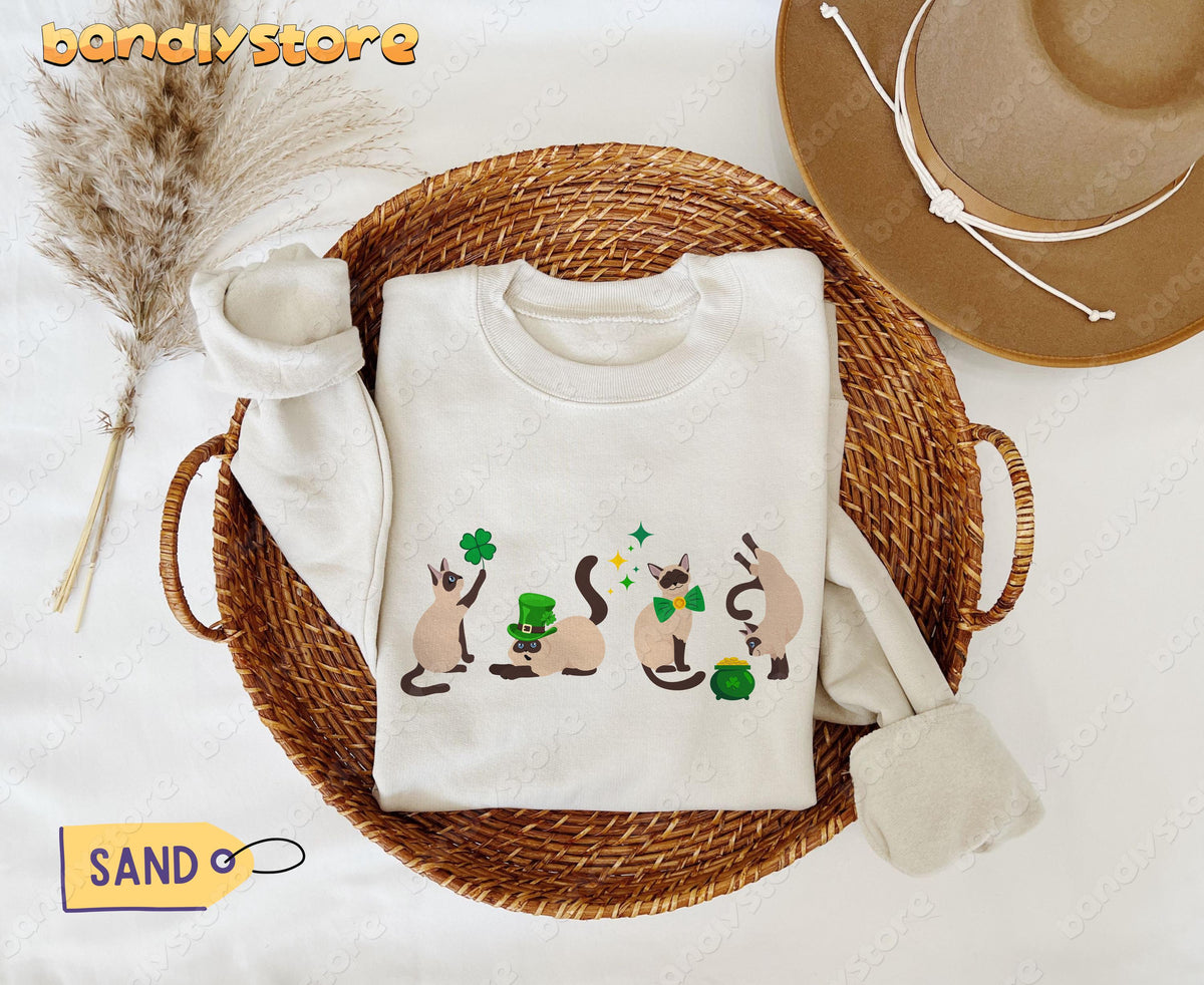 Siamese Cat St Patrick's Day Sweatshirt in Sand, folded in a round wicker basket beside pampas grass and a brown hat.