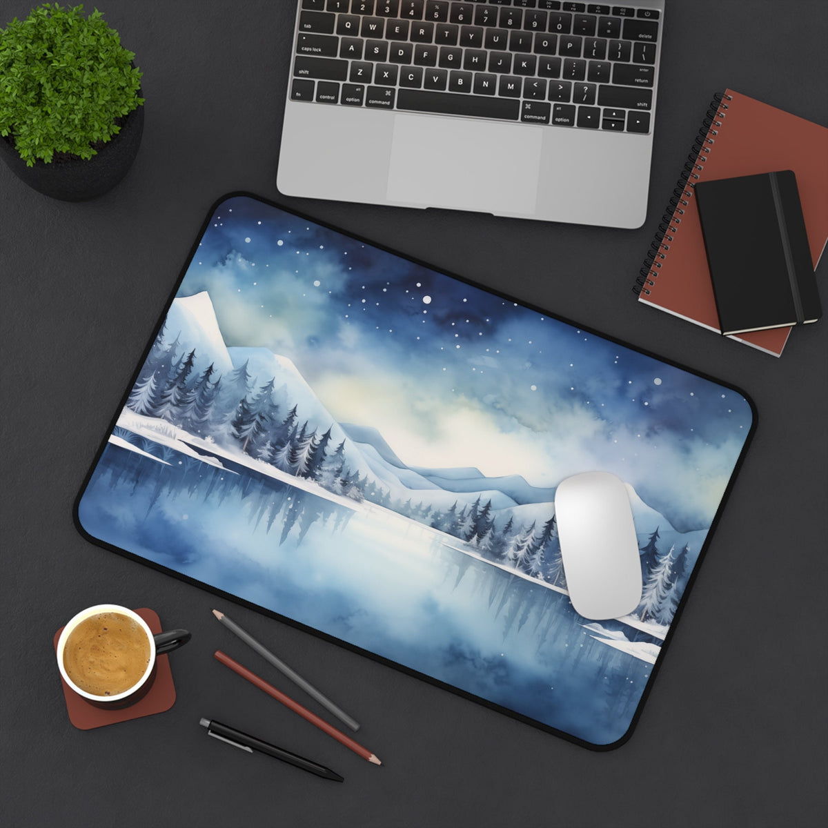 Snow Mountains Desk Mat in 12 × 18 inches on a dark desk with laptop, plant, coffee, and notebooks.