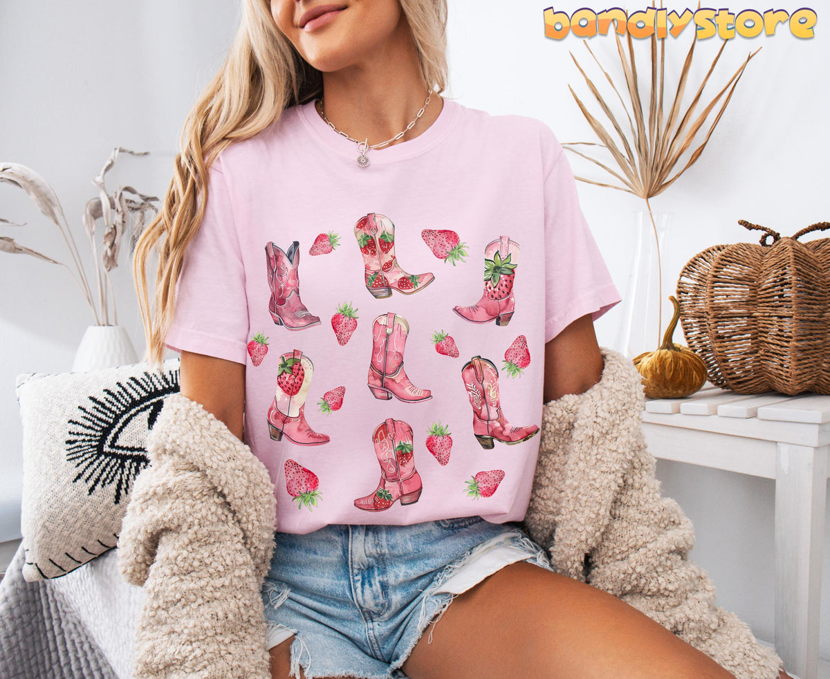 Strawberry Cowgirl Boots T-Shirt in Blossom on seated model amid dried plants, pillows and woven baskets.