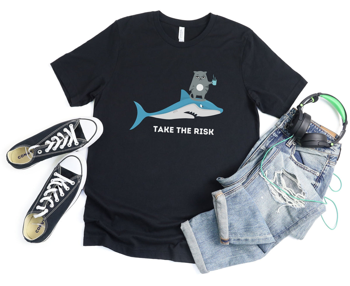 Take The Risk Funny Cat T-Shirt black flat lay with sneakers left, ripped jeans and headphones right.