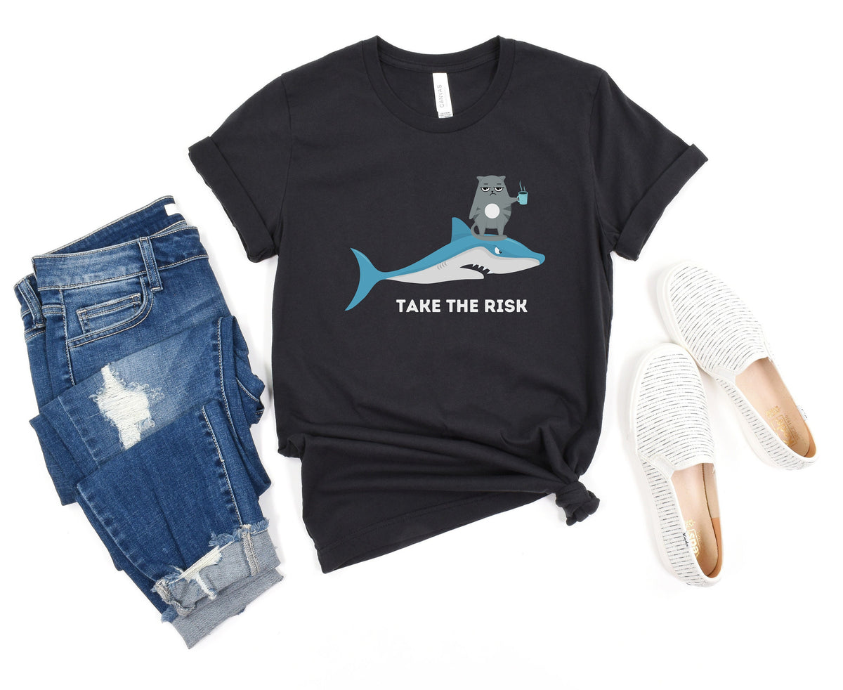 Take The Risk Funny Cat T-Shirt black flat-laid beside ripped jeans and white slip-on shoes.