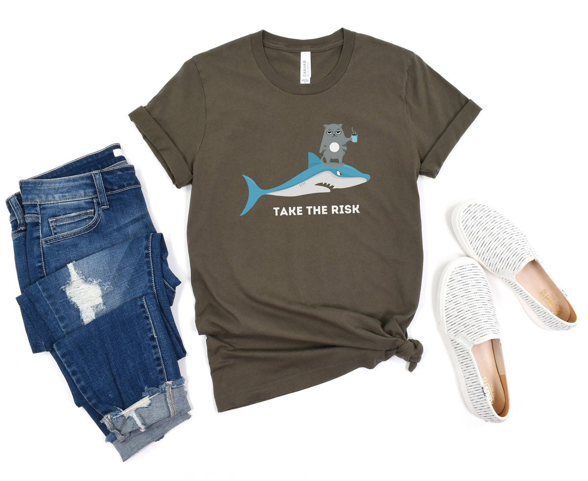 Take The Risk Funny Cat T-Shirt in olive, overhead flat lay beside folded jeans and white slip-ons.