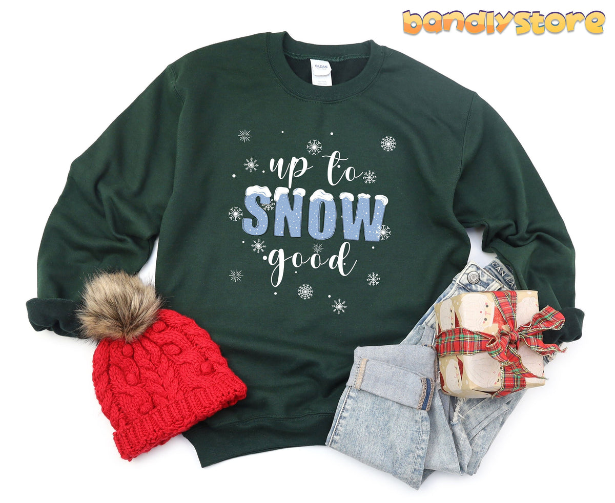 Up To Snow Good Sweatshirt in forest green flat lay with beanie, jeans and wrapped gift.