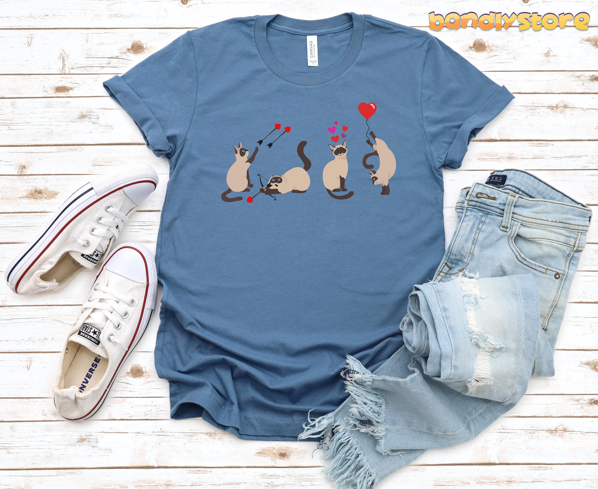 Valentine's Day Siamese Cat T-Shirt steel blue flat on wooden surface beside white sneakers and ripped jeans.