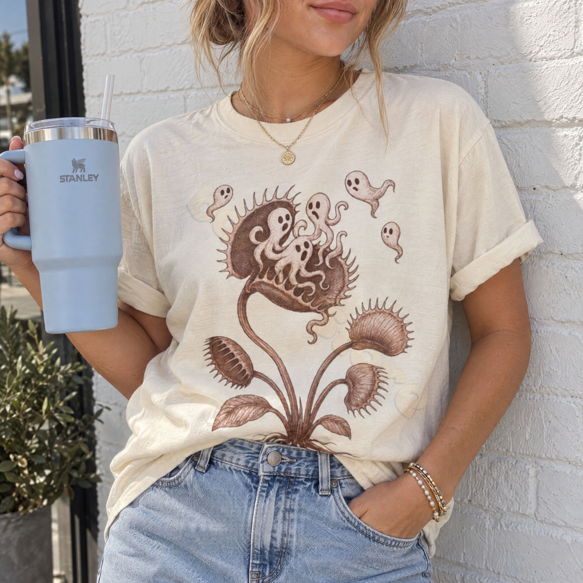 Vintage Ghost Eating Flytrap T-Shirt in ivory worn front view by a person holding a tumbler against a white brick wall.