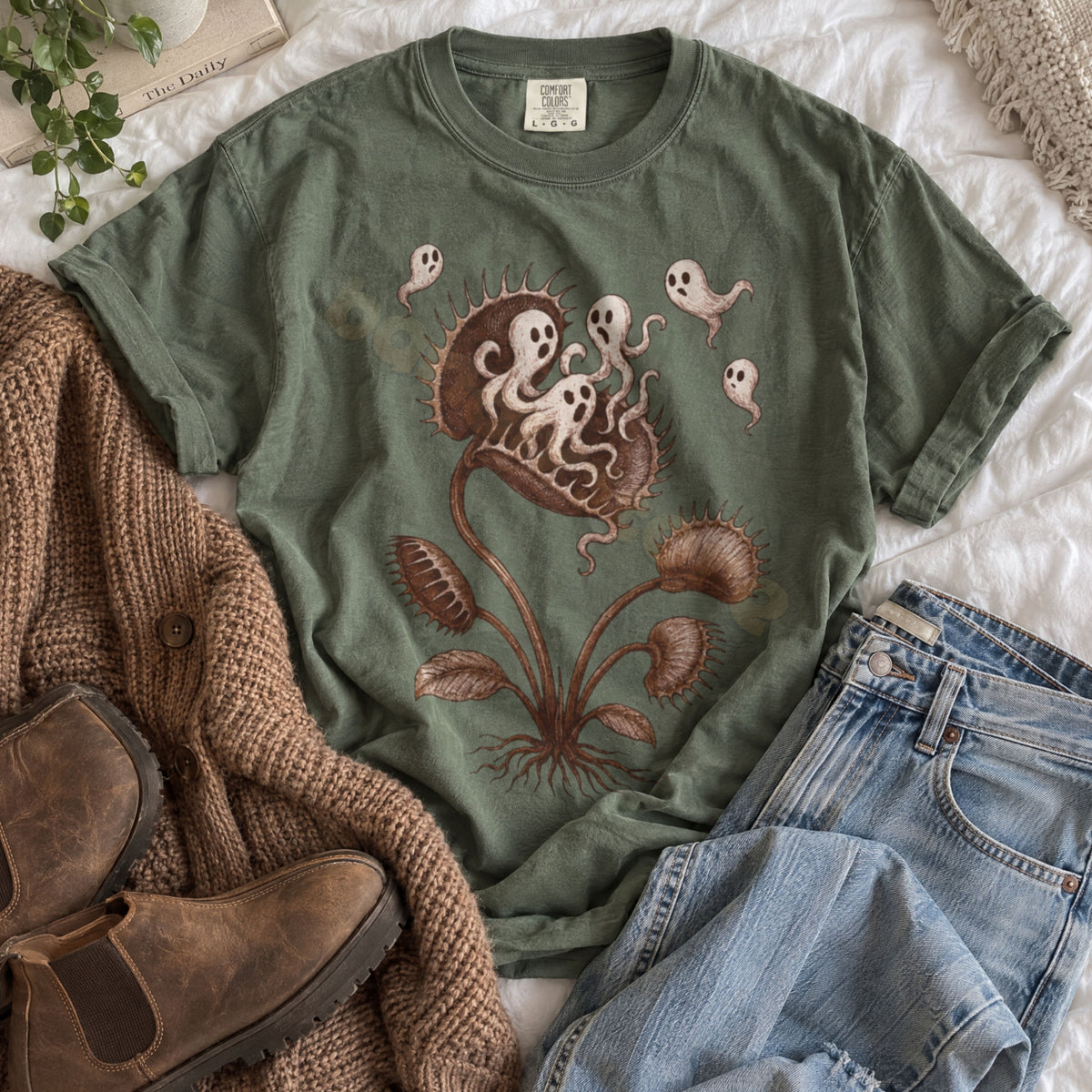 Vintage Ghost Eating Flytrap T-Shirt in moss laid flat on white bedding beside boots, a sweater, and jeans.
