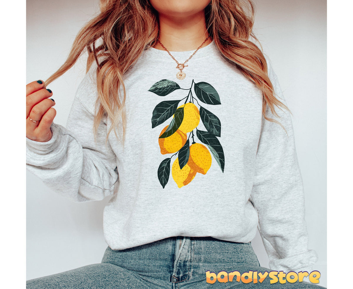 Vintage Lemons Sweatshirt in ash, cropped view of person seated against plain backdrop, lemon branch print centered on chest.